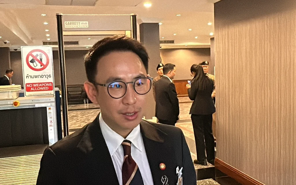 Man wearing glasses and a suit in a building lobby near a security scanner.