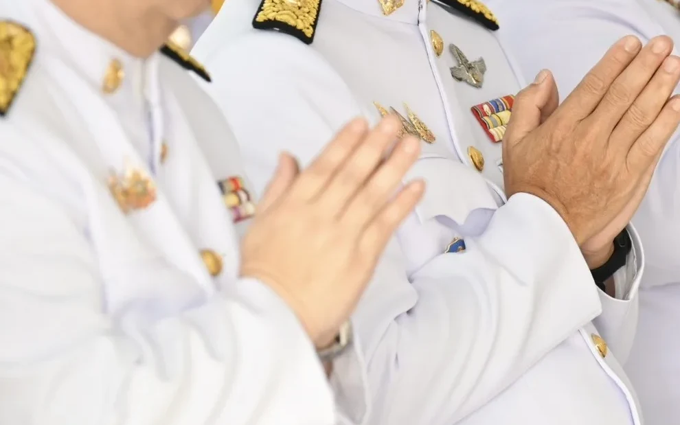 Officials in white uniforms perform a wai greeting.