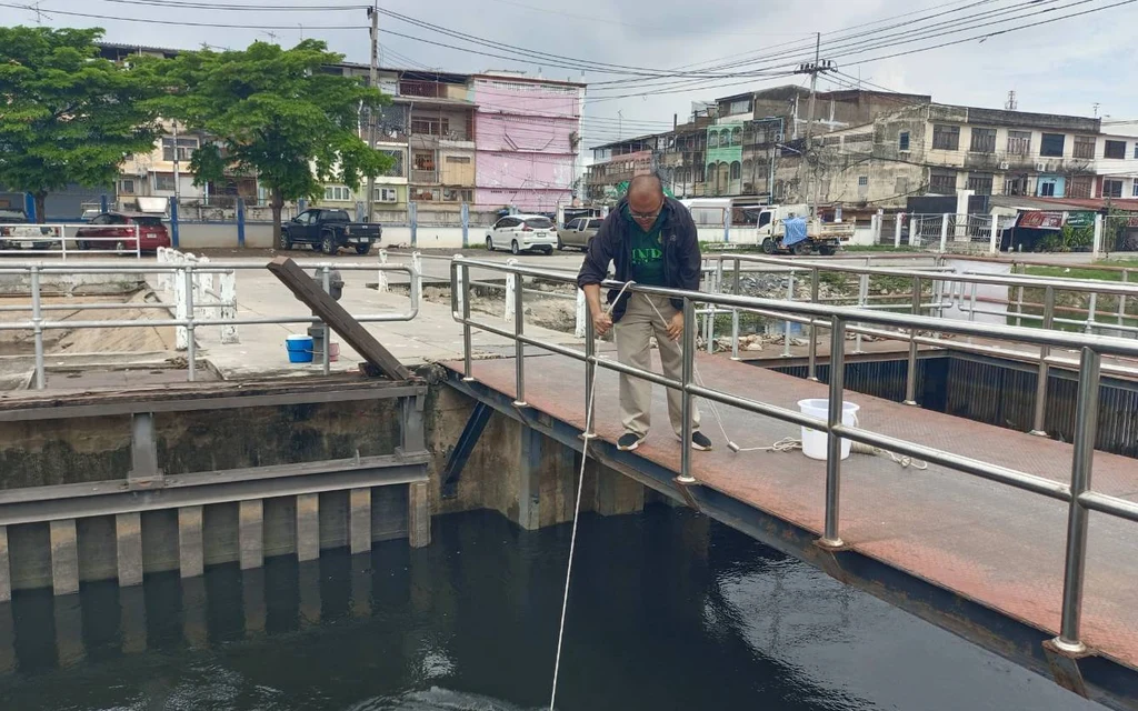 An official collecting water samples from a canal for quality testing.