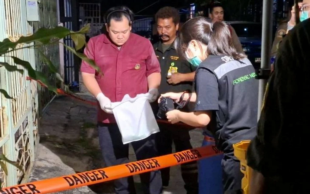 Investigators examine a bag at a house gate behind danger tape.