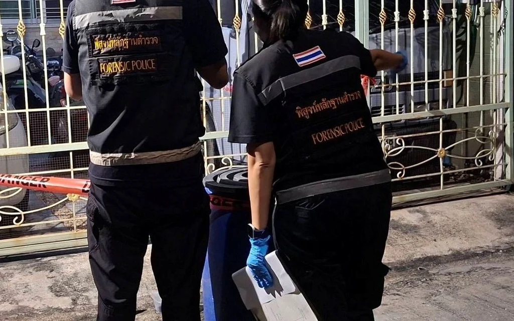 Forensic police officers inspect a gated Bangkok house at night.