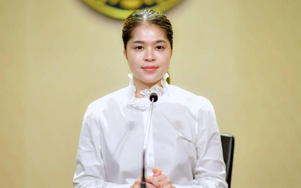 Woman in white speaking at a microphone during a press event