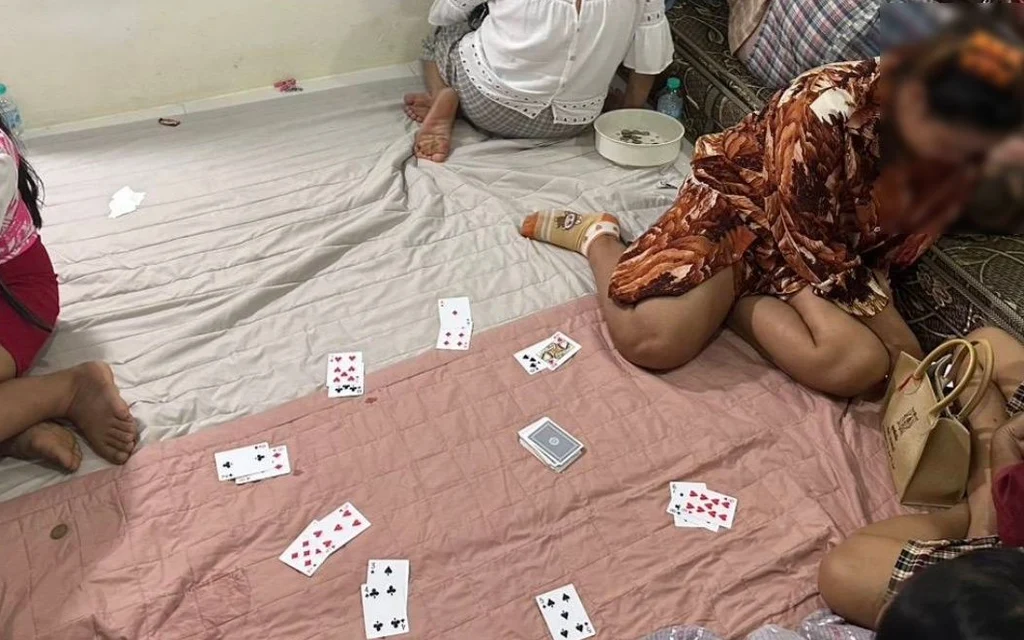 People sitting on the floor playing cards during a gambling raid.