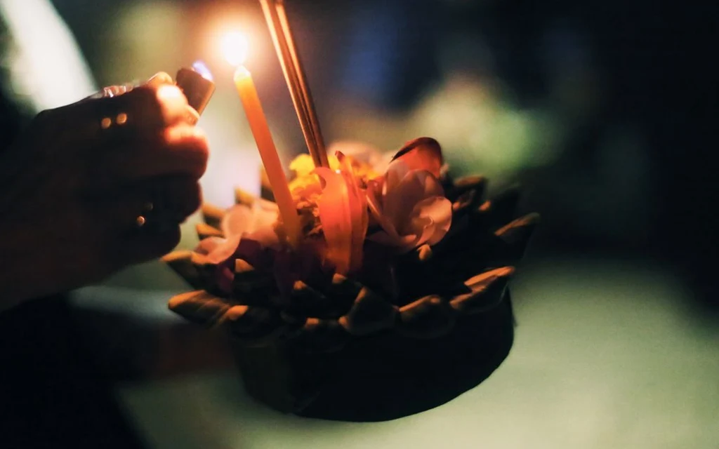 A person lighting a candle on a traditional Loy Krathong krathong.
