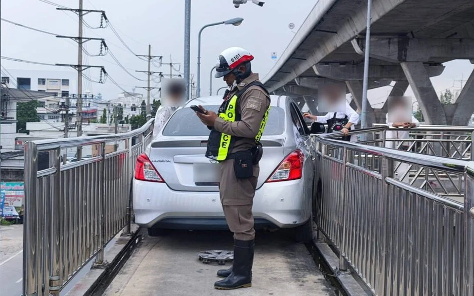 A police officer inspects a car stuck on a motorcycle bridge.