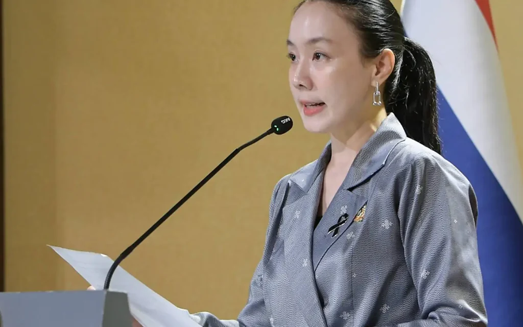 A woman speaks at a podium beside the Thai flag.