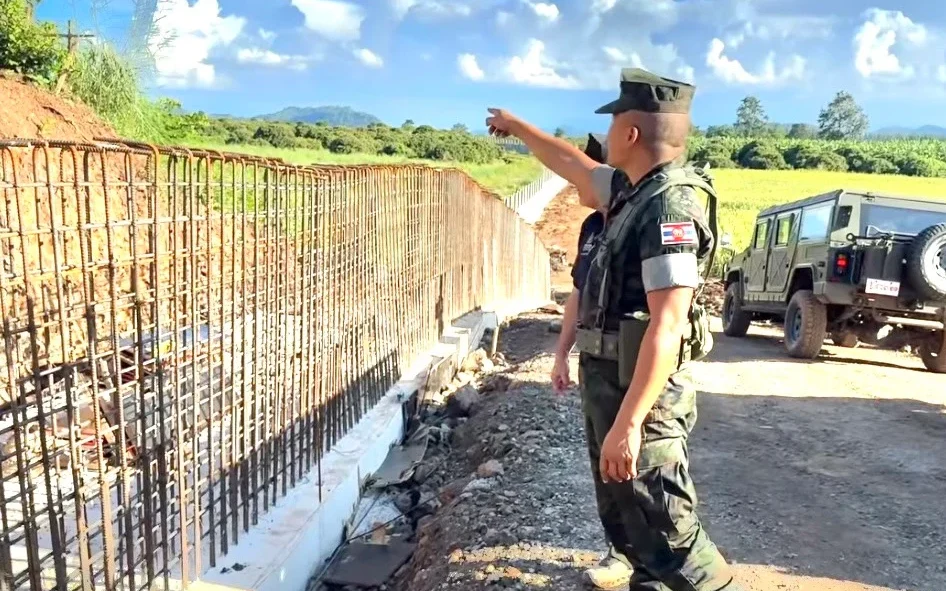 Officials inspect a border fence construction site beside parked vehicles.