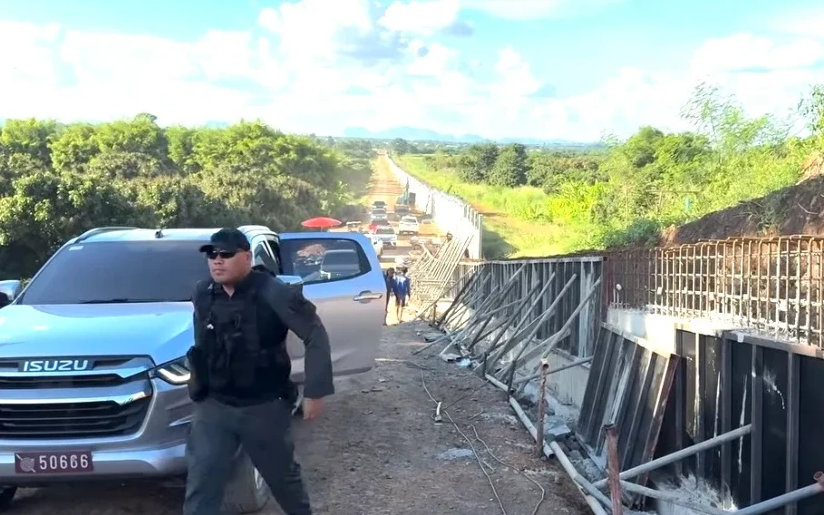 A man stands beside a pickup near border fence construction.