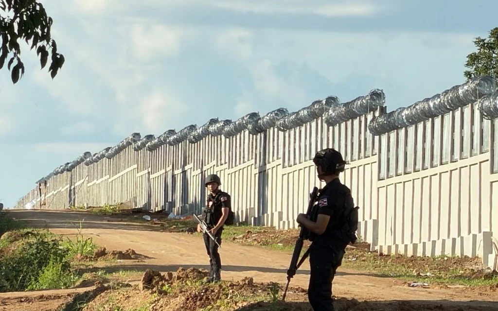 Two armed uniformed officers patrol beside a newly constructed border fence.