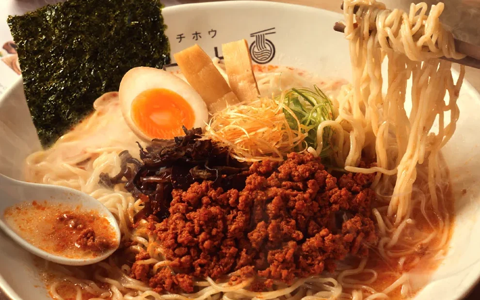 A bowl of ramen with noodles, egg, seaweed, and minced meat.
