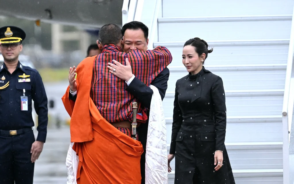 Anutin embraces a monk beside an aircraft stairway as officials look on.