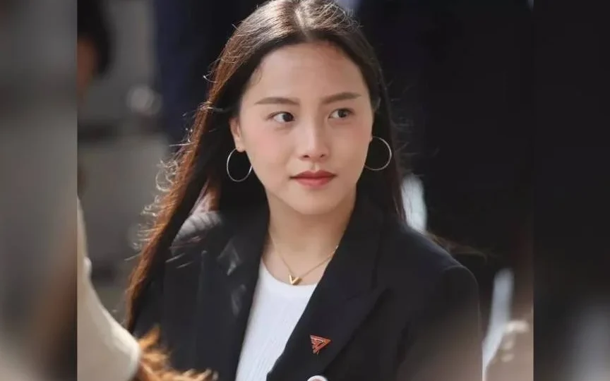 A woman in a black blazer photographed outdoors.