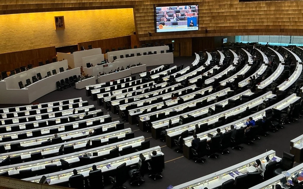 Wide view of an empty parliamentary chamber with a few seated attendees.