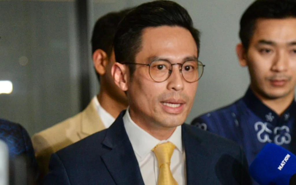 A suited man speaks to reporters alongside several other men.