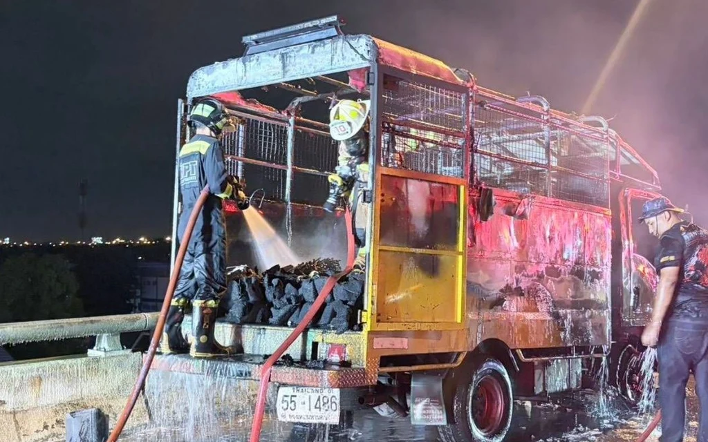 Firefighters extinguishing a fire on a road painting truck at night.