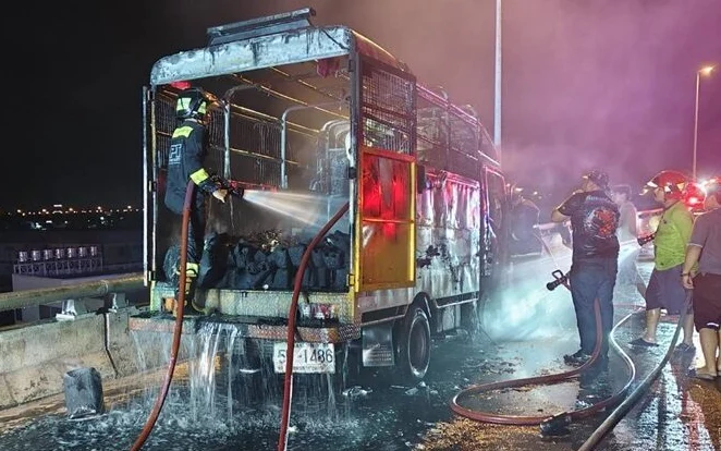 Firefighters extinguishing a fire on a road painting truck at night.