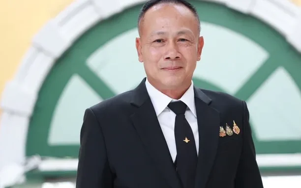 A man in a black suit poses in front of a green arch.