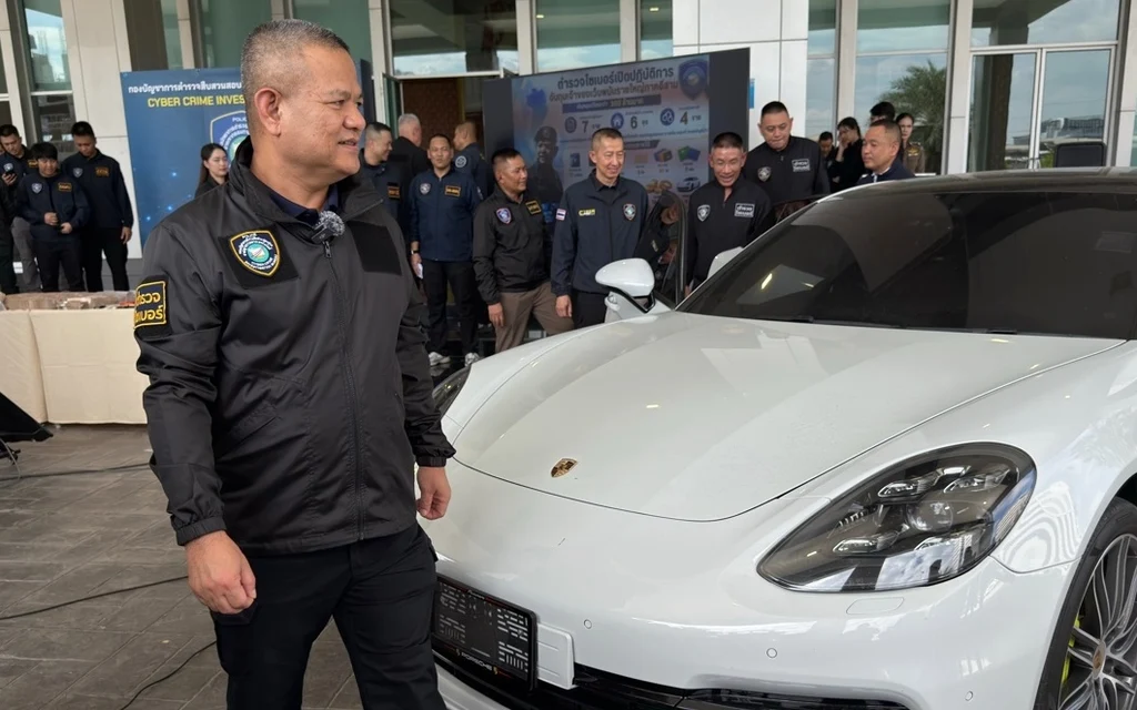Thai police officers standing with a seized white luxury car.