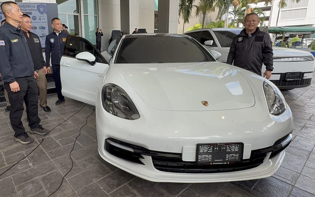 Police officers standing next to a seized white luxury car.