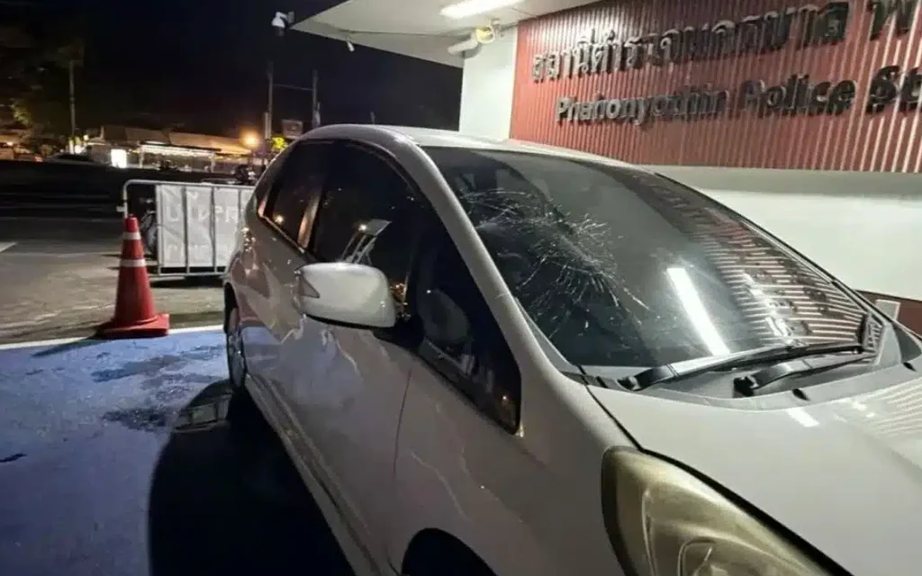 White car with shattered windshield outside a police station at night.