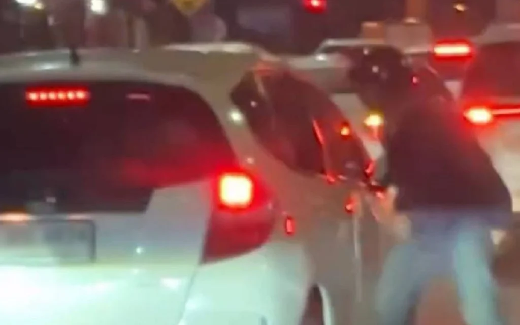 A person stands beside a car in nighttime traffic.