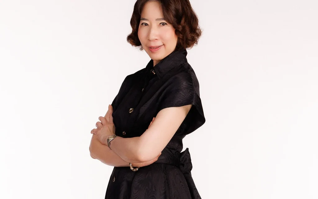 Woman in black formal attire posing against a plain white background.