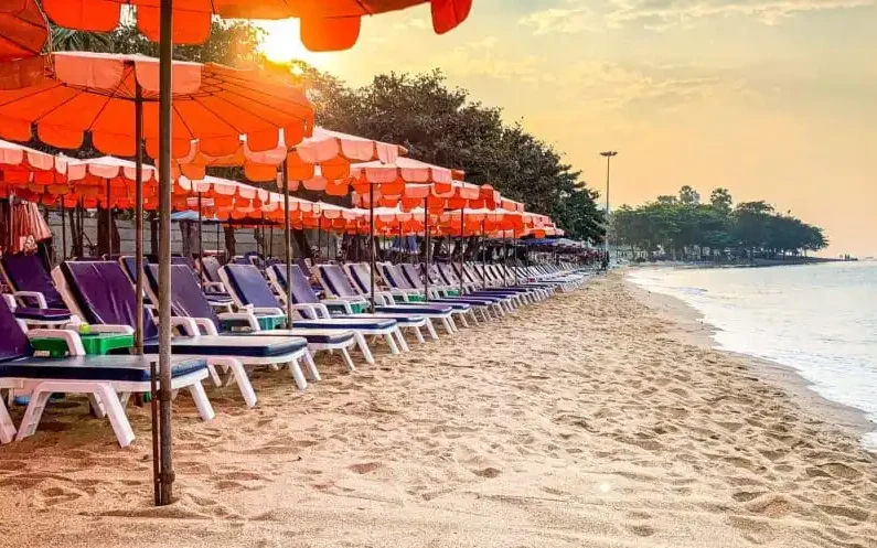 Empty beach lined with orange umbrellas and lounge chairs at sunset.