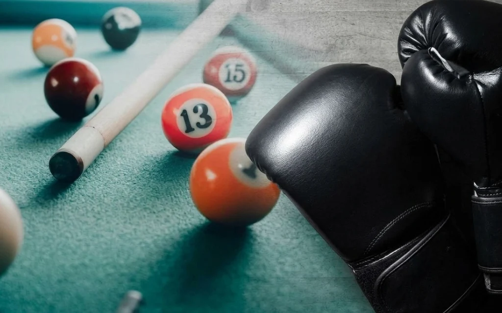 Black boxing gloves beside billiard balls and a cue on a pool table