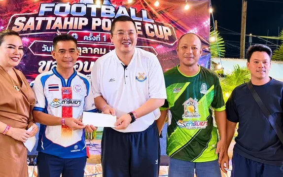Five adults pose at a football cup event holding a cheque.