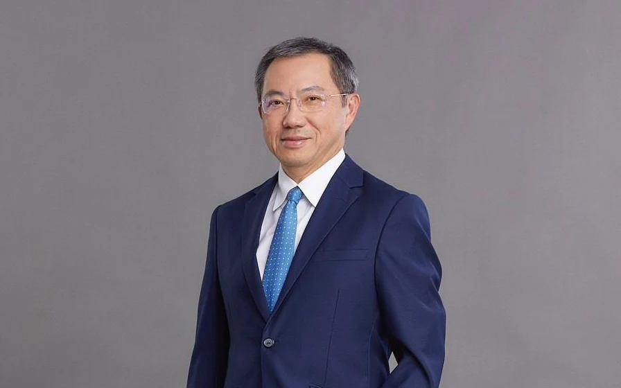 A man in a navy suit and blue tie against a gray background.