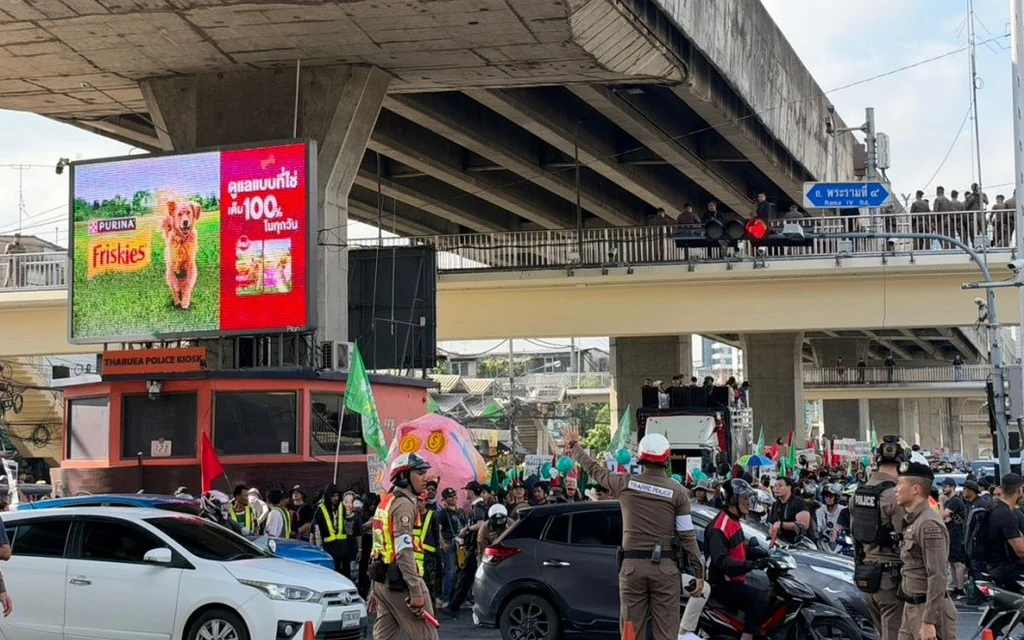 Protesters and police at Rama IV intersection with a large billboard.