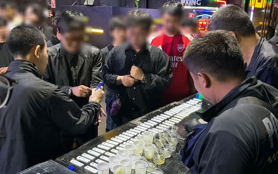 Close up of seized drug equipment and cups surrounded by blurred people and officers