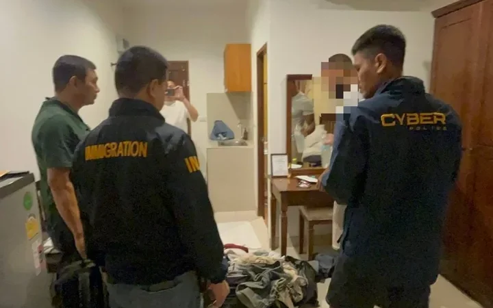 Officers inspect belongings during a suspected scammer arrest in a room.