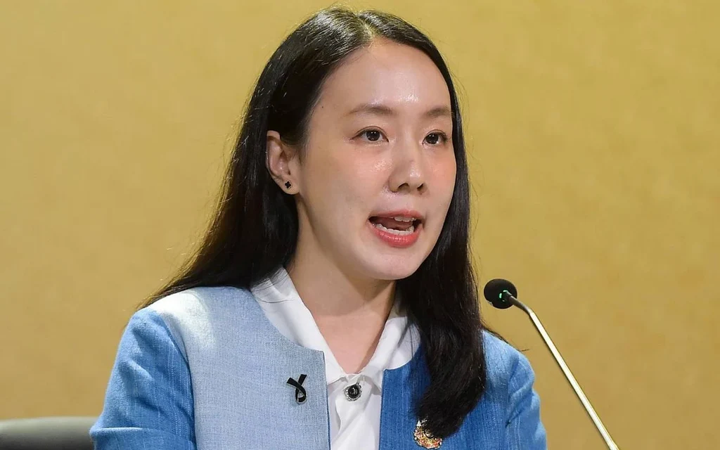 Woman speaking at a microphone against a yellow background
