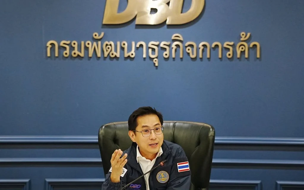 Thai commerce official speaks at a table beneath the Department of Business Development sign.