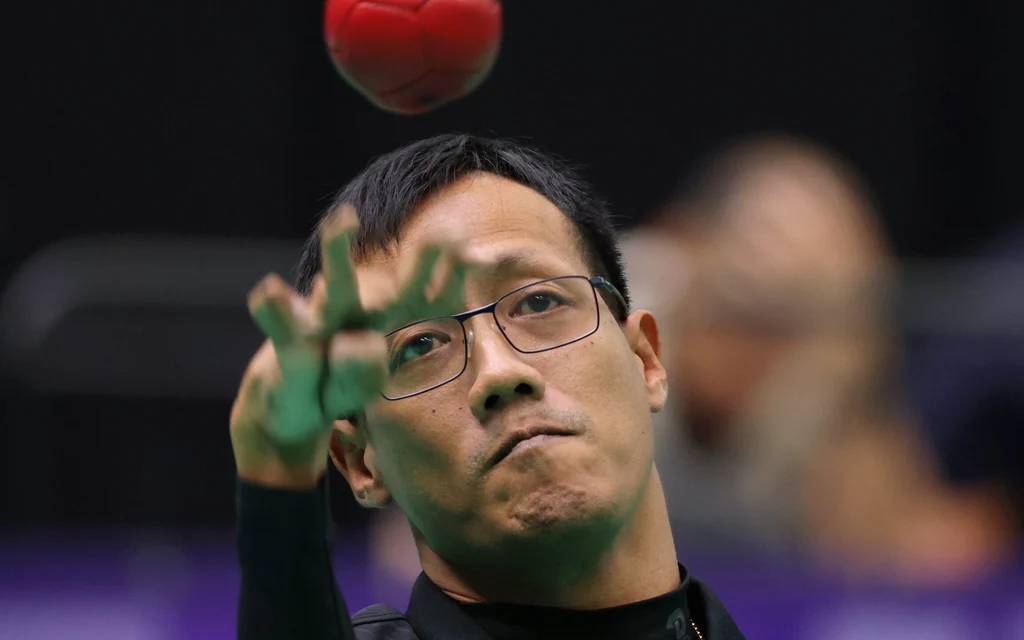 A man in glasses tosses a red ball during a sporting event.