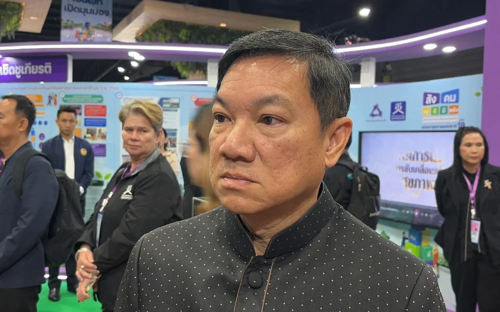 Man in a black jacket at a crowded exhibition booth.