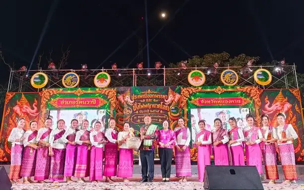 Officials and dancers pose on a brightly decorated festival stage at night.