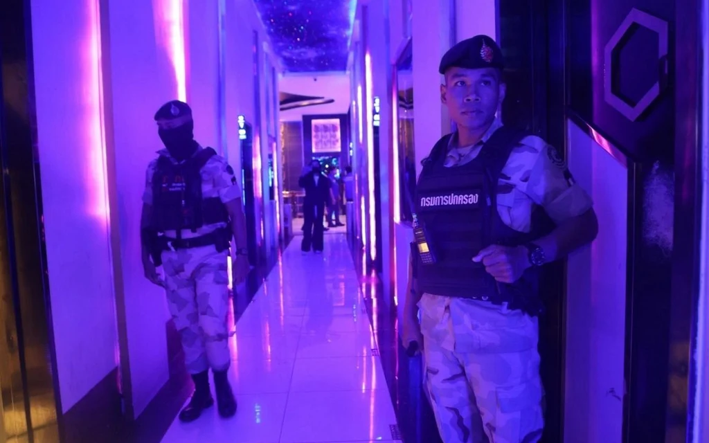 Uniformed officers stand in a brightly lit KTV hallway during a raid.