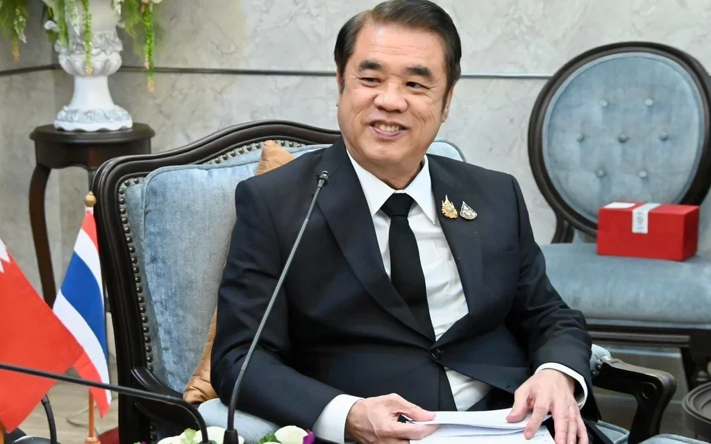 A suited man sits in a meeting room beside national flags.
