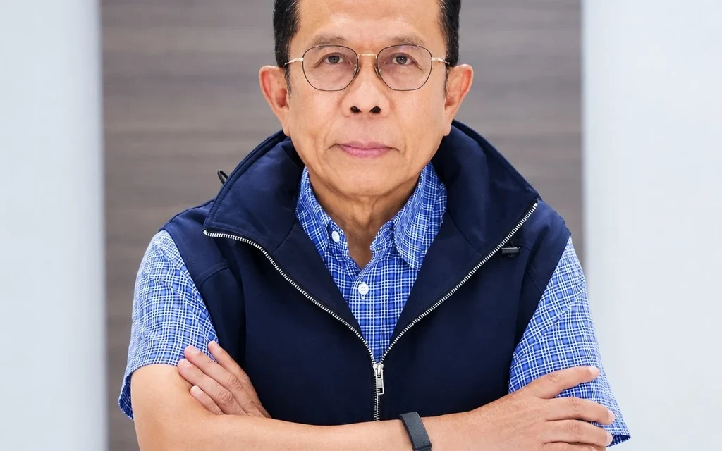 A man wearing glasses and a navy vest poses with arms crossed.