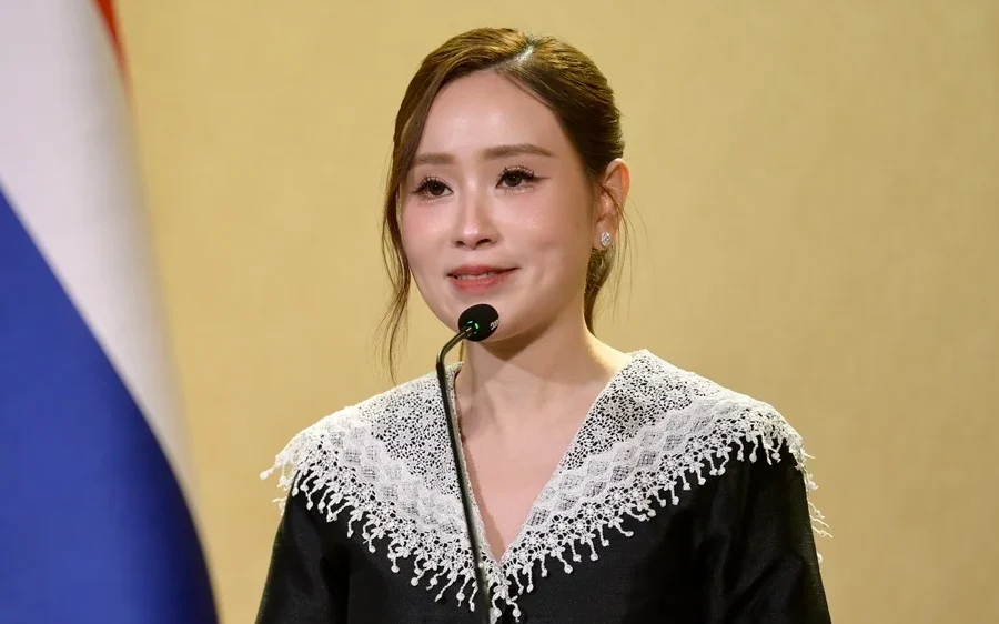 A woman speaking at a podium with a Thai flag background.
