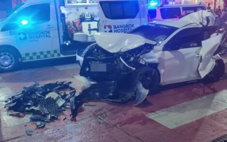 A badly damaged car at a nighttime crash scene with ambulances nearby.