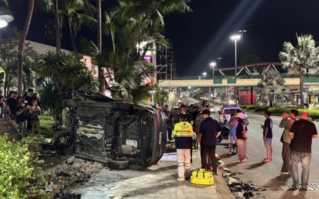 Overturned burned vehicle at a nighttime crash scene with responders and bystanders.