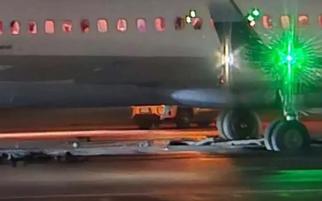 Airplane stopped on runway at night, with landing gear and green lights visible.