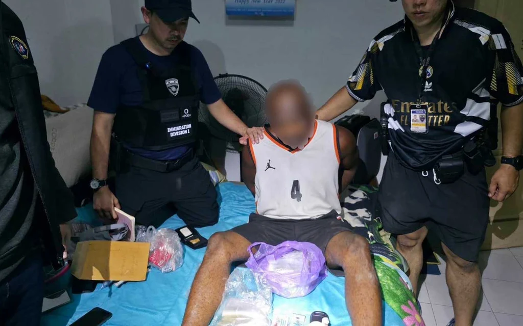 Police detaining a man sitting on a bed surrounded by drugs