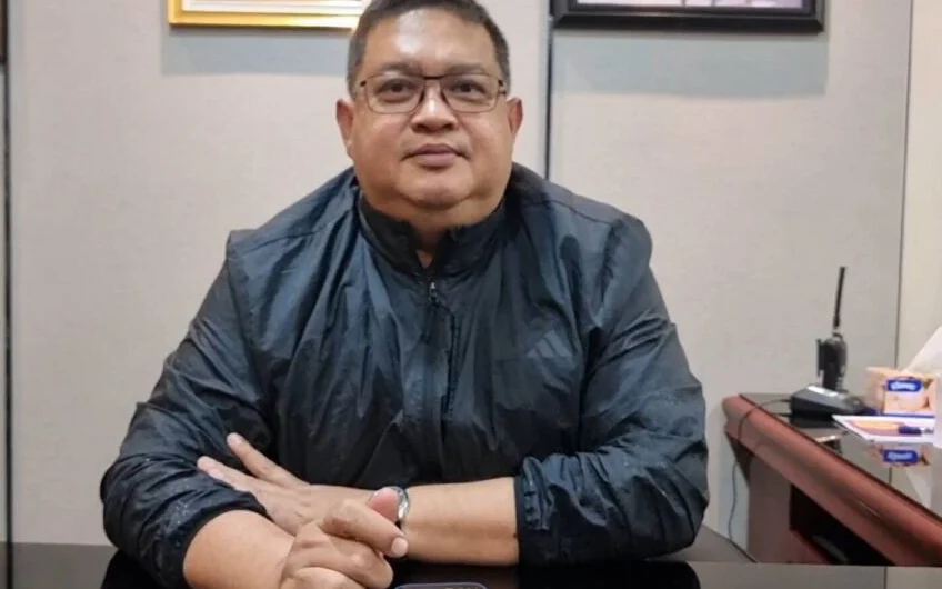 A man in a black jacket sitting at a desk.