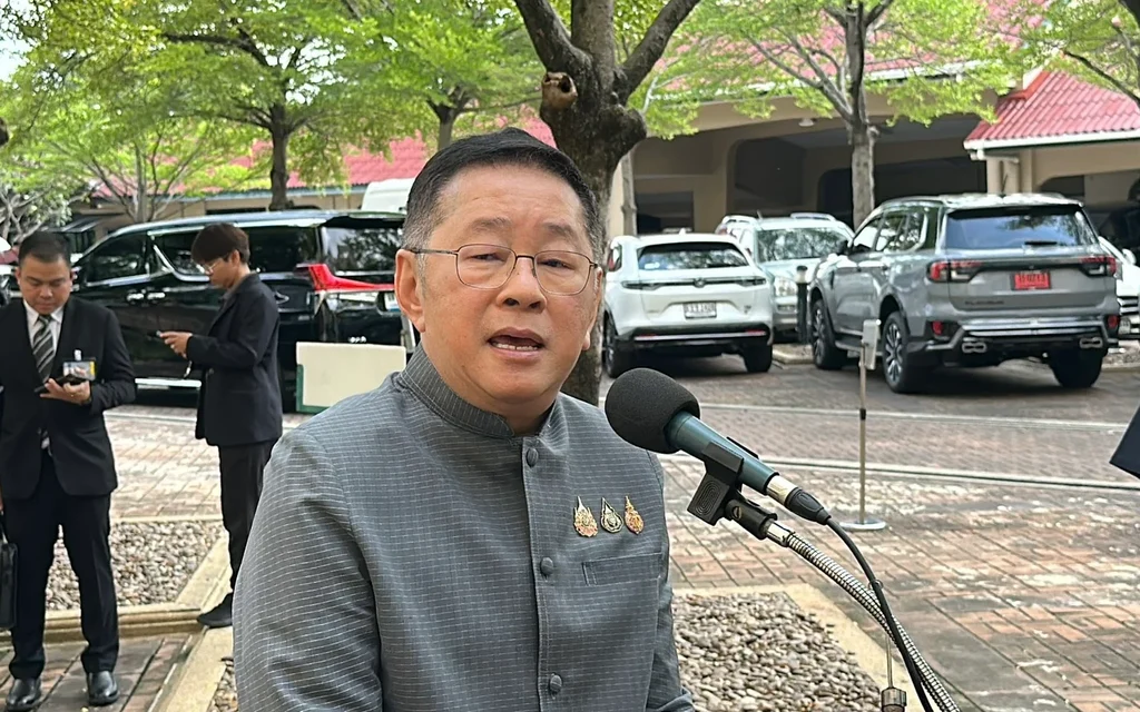 Man speaks to reporters outdoors near parked vehicles.