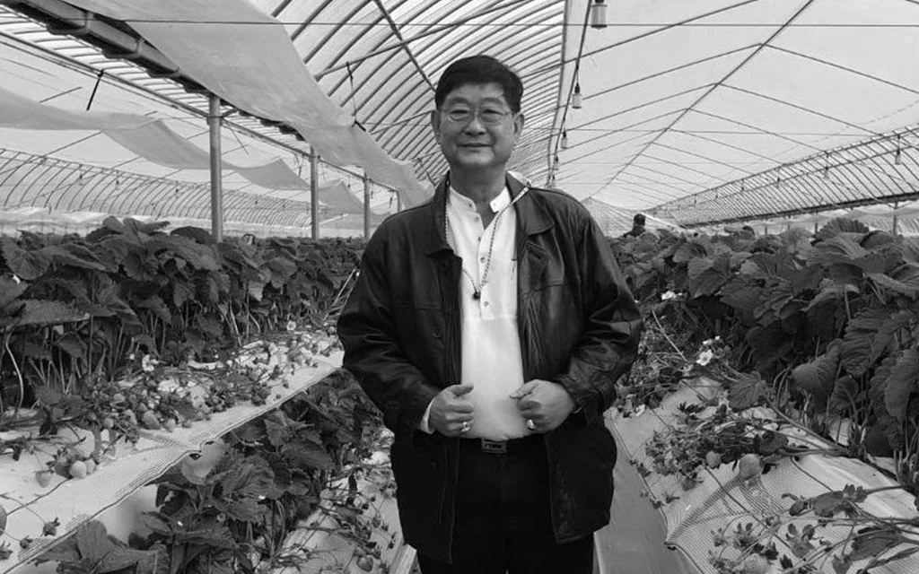 Black-and-white photo of a man standing among greenhouse crops.