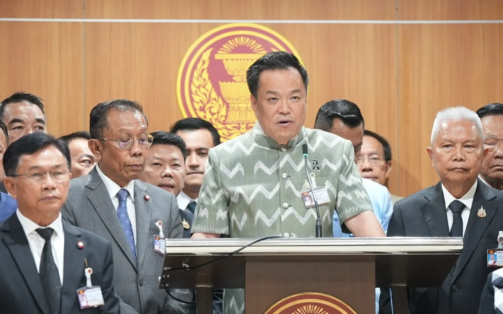 Anutin speaks at a parliamentary podium surrounded by officials.